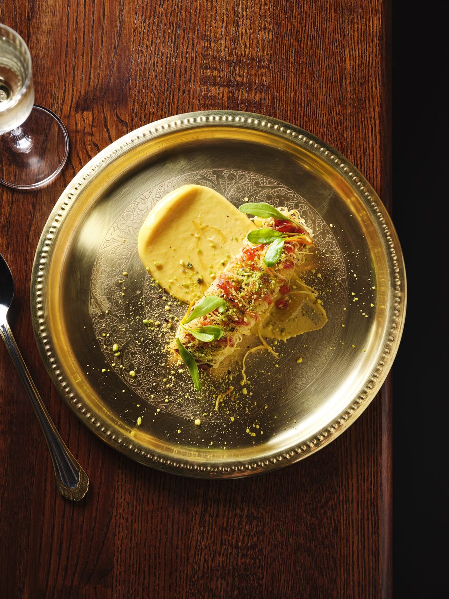 A saffron and pistachio dessert plated on a brass thali at GOAT, Auckland